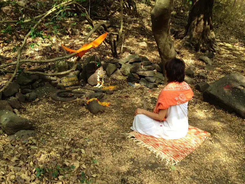 Eine Frau sitzt auf einer Decke vor einem kleinen Waldschrein in Indien